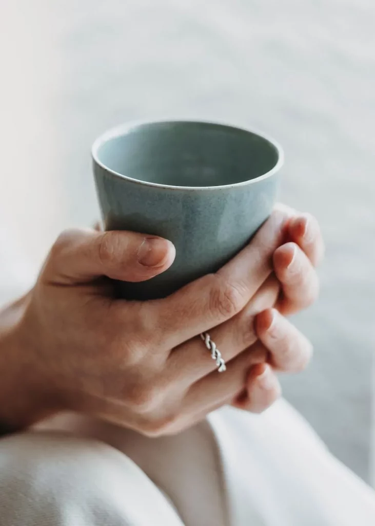 Hände halten Tasse in ruhiger Atmosphäre, Nahaufnahme mit Ring und weichen Naturtönen